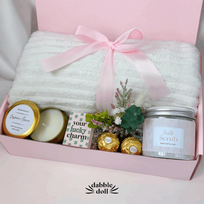 Dabble Doll gift box for women featuring a soft white blanket, candles, and beauty products in pink packaging