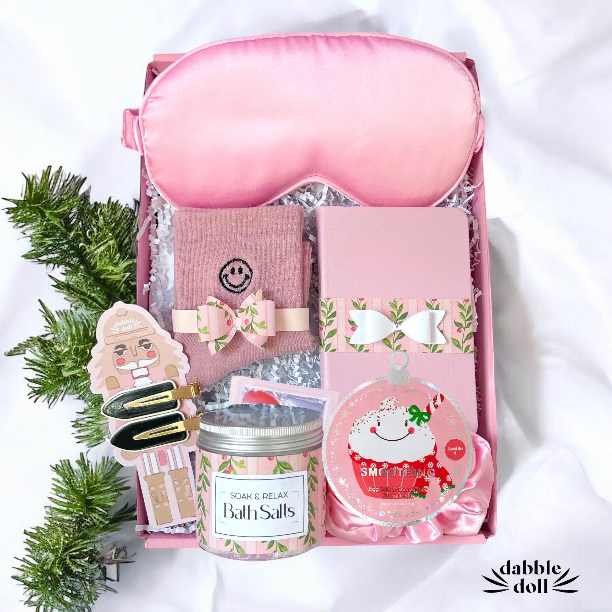Pink gift box filled with relaxing items for women including bath salts, sleep mask, and cozy accessories