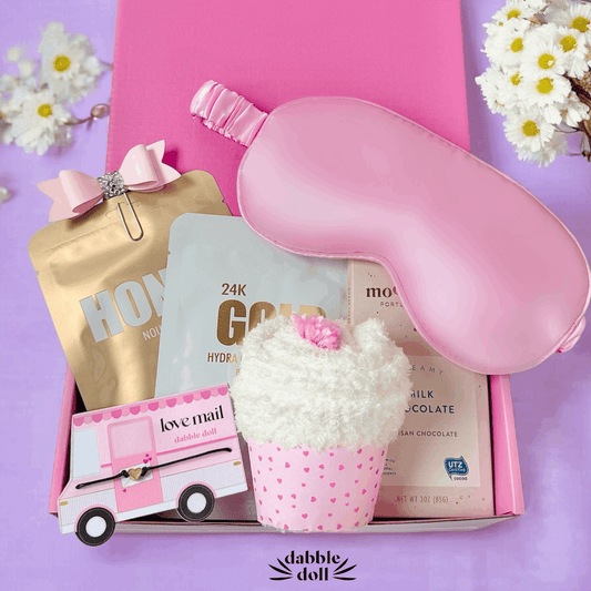 Dabble Doll gift box containing a pink eye mask, treats, and love mail card featuring a cupcake