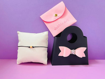 Dabble Doll Gold heart bracelet on a white pillow with a pink bow accessory bag for girls and women