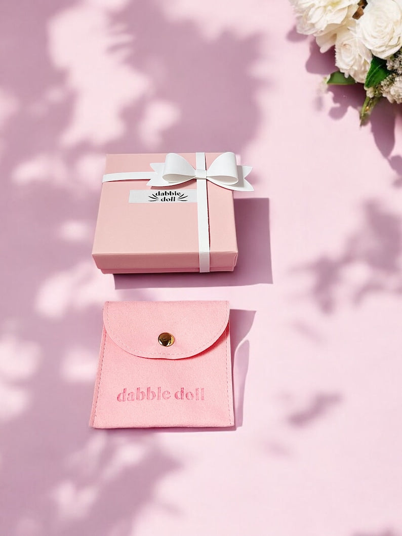 Pink gift box with white ribbon and a pink wallet for girls featuring a gold heart design