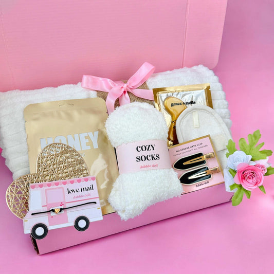 Dabble Doll hygge gift box for her with cozy socks, honey packets, hair clips, and decorative flowers in a pink gift box