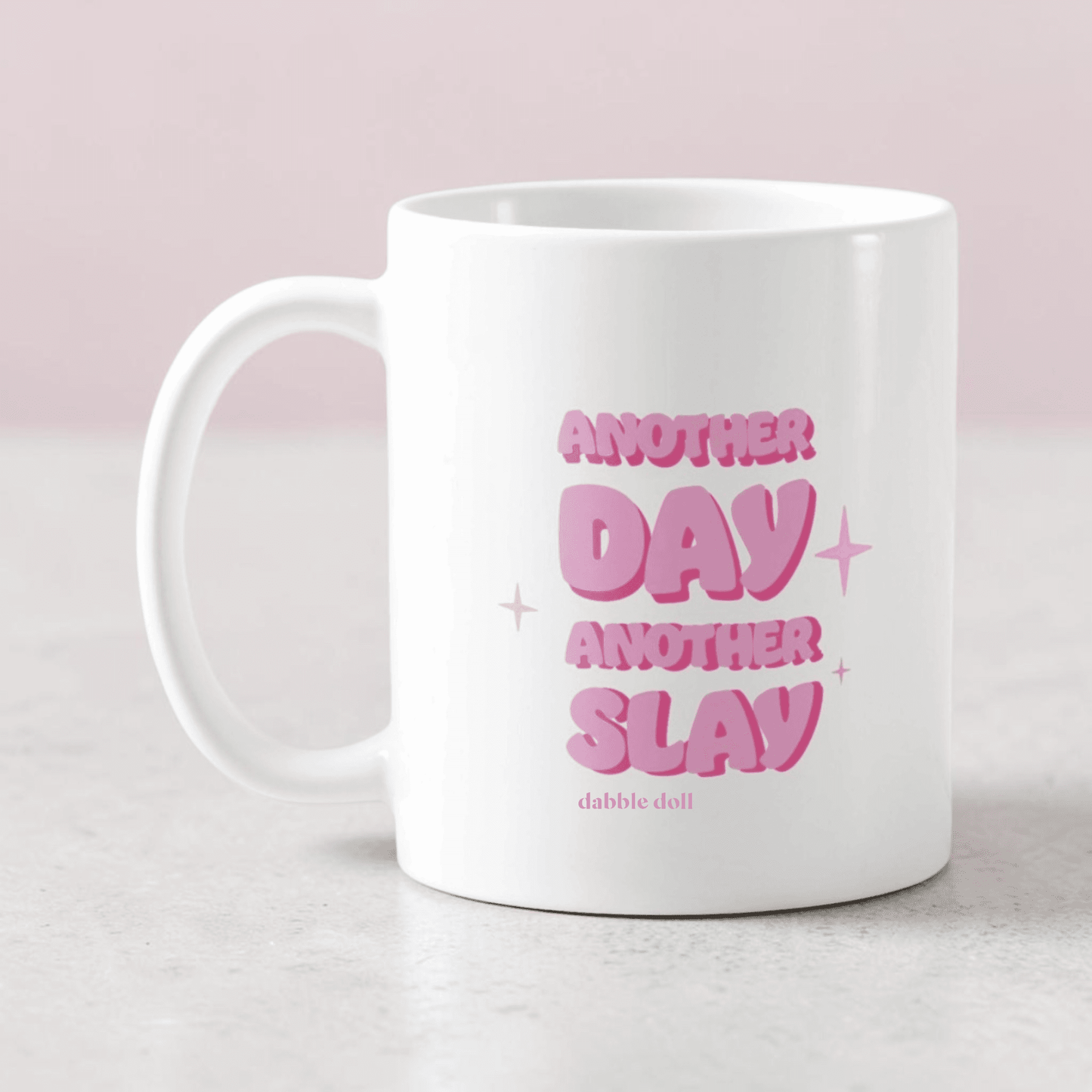 White mug featuring the phrase Another Day Another Slay in pink, by Dabble Doll