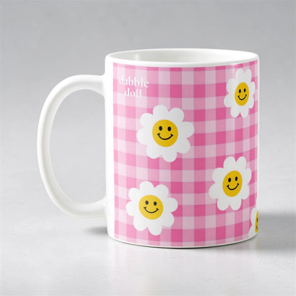 Dabble Doll smiley face mug with cheerful daisies on a pink checkered background