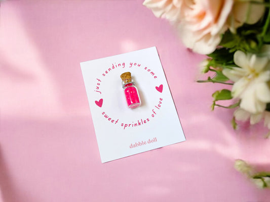 Pink Dabble Doll sprinkles in a glass vial on a card, perfect for girls and women crafting projects