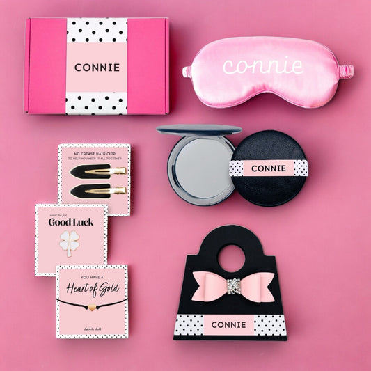 Pink gift box for women containing a sleep mask, hair clips, and beauty products