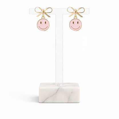 Dabble Doll pink smiley face earrings with gold bow accents for a cheerful accessory