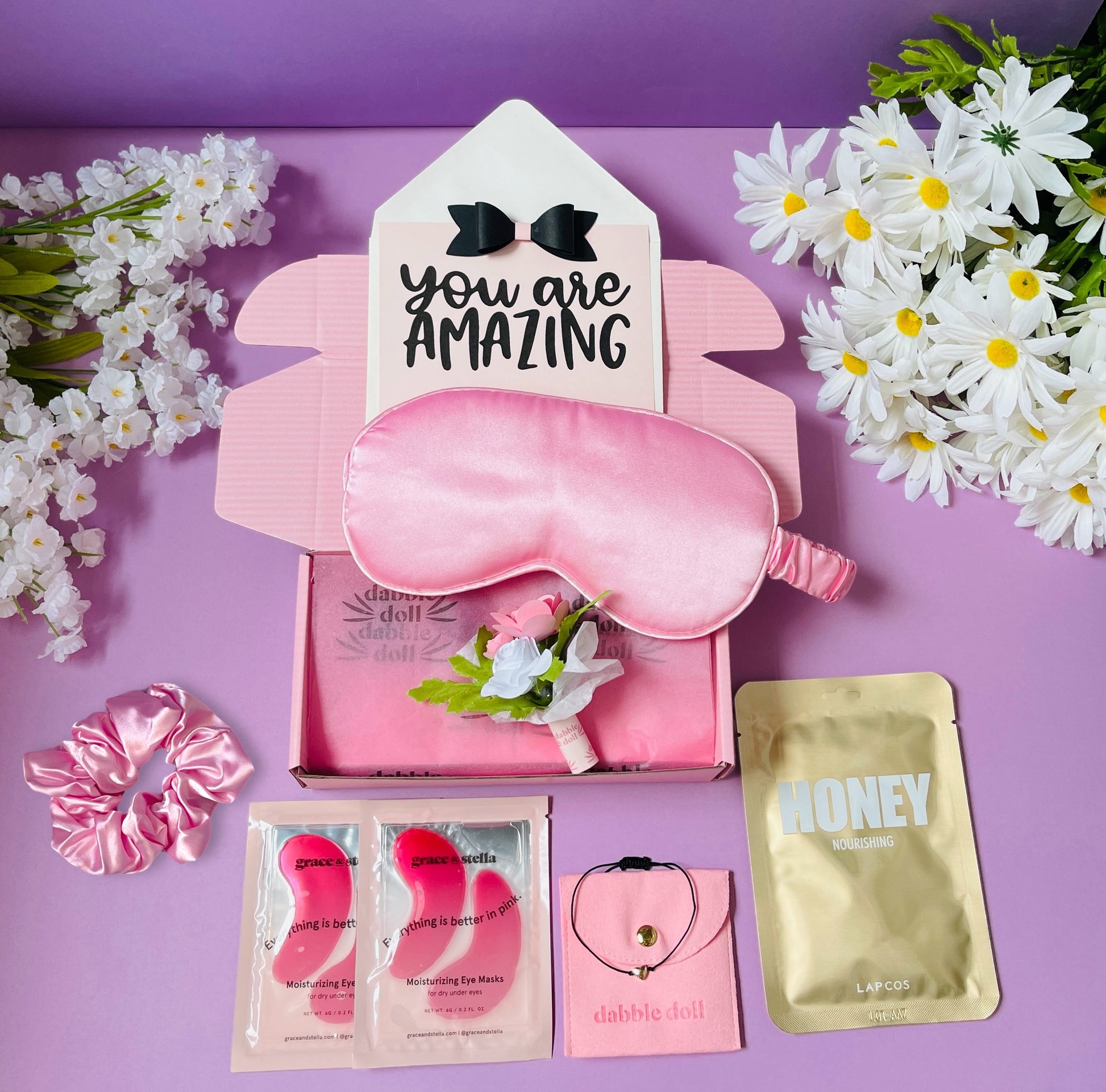Pink Dabble Doll gift box for women featuring a sleep mask, hair scrunchie, and skincare items