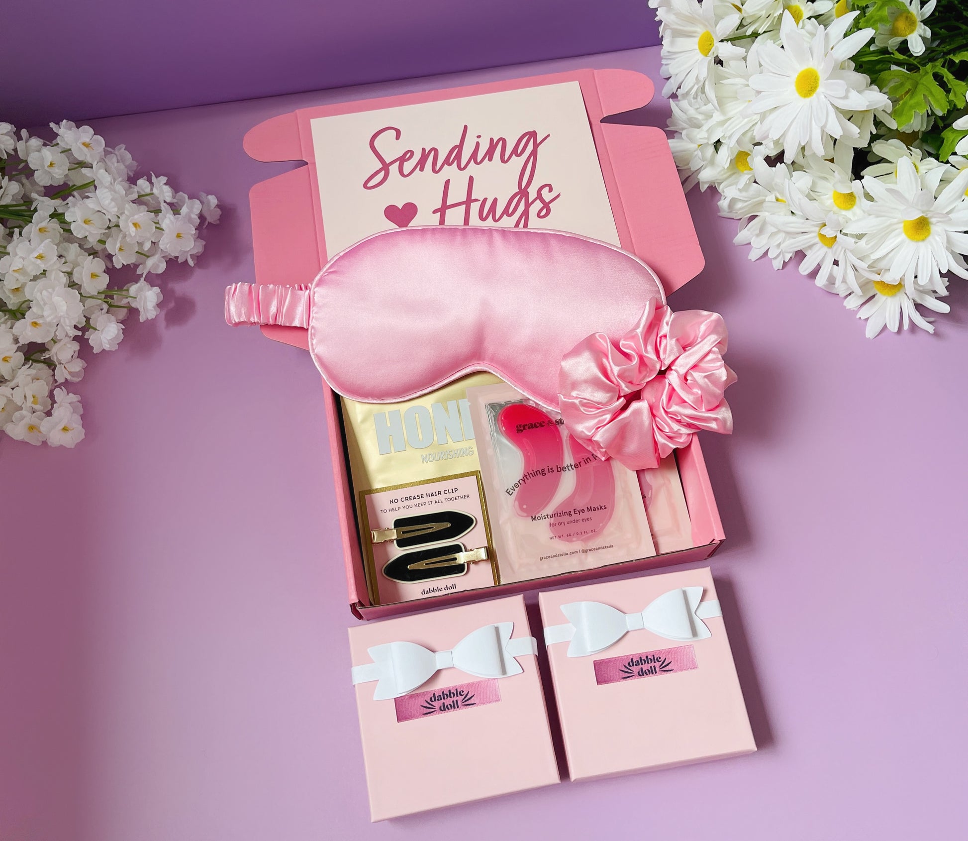 Pink gift box for women featuring a silk sleep mask, beauty products, and floral accents