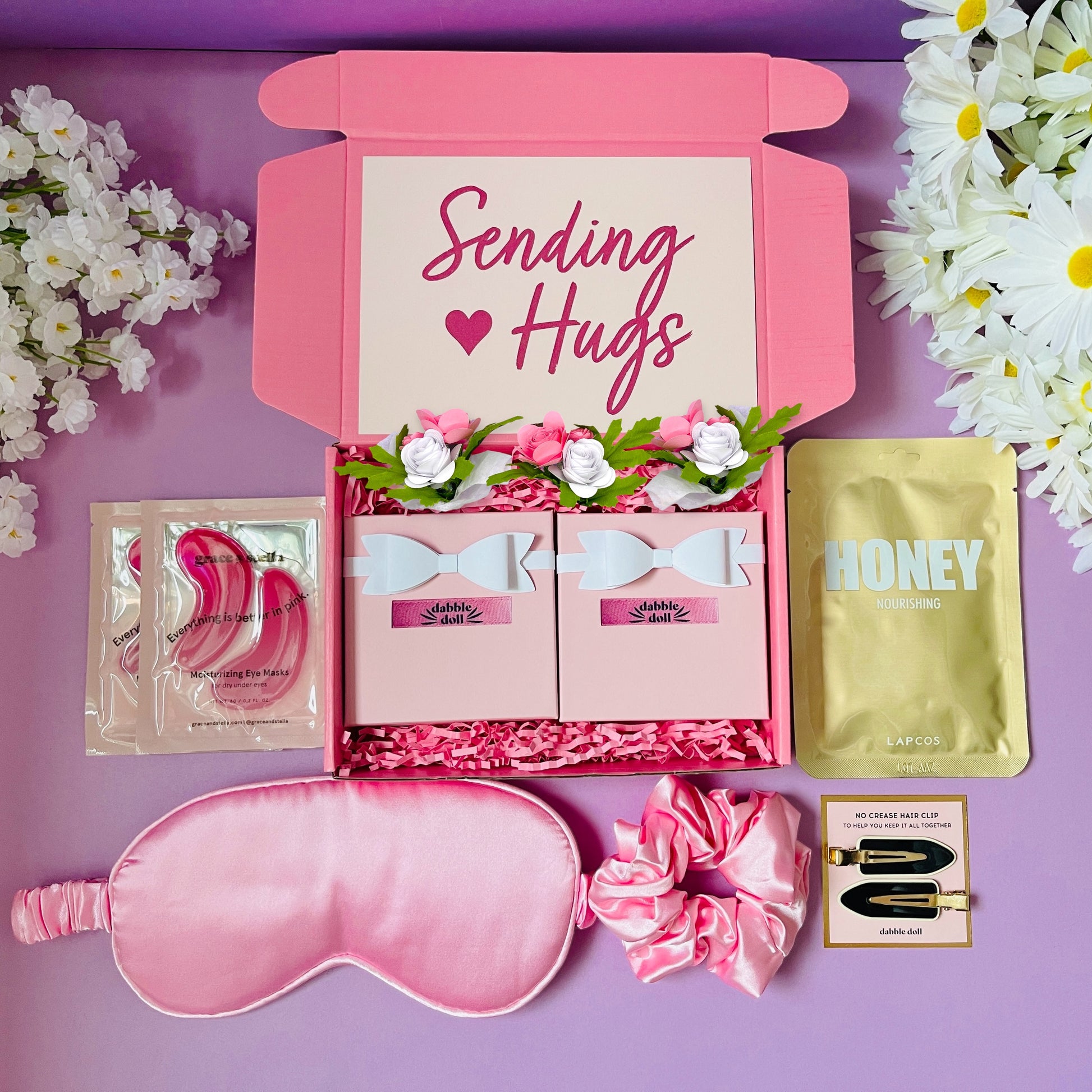 Pink gift box for women featuring sleep mask, scrunchie, and skincare items with floral accents