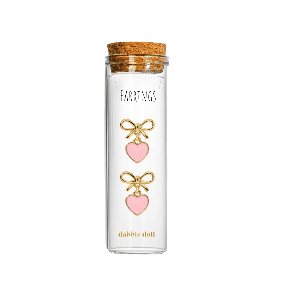 Dabble Doll heart earrings in pink with gold bow details in a glass tube packaging