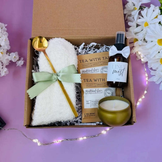 Dabble Doll hug in a box gift set with cozy socks, golden spoon, tea packets, linen mist, and candle in a brown gift box
