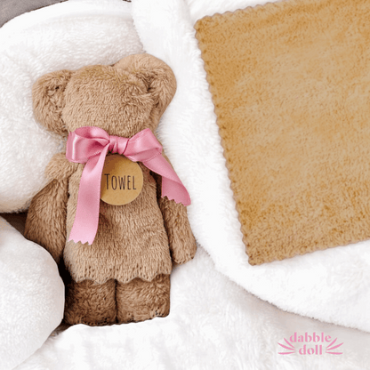 Dabble Doll hygge gift box for women featuring a soft teddy bear towel with pink ribbon and cozy blanket