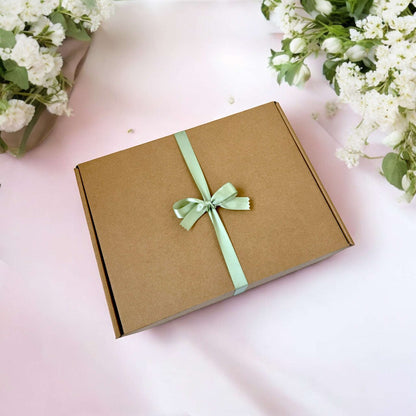 Dabble Doll hygge gift box with green ribbon bow on brown cardboard surrounded by white flowers