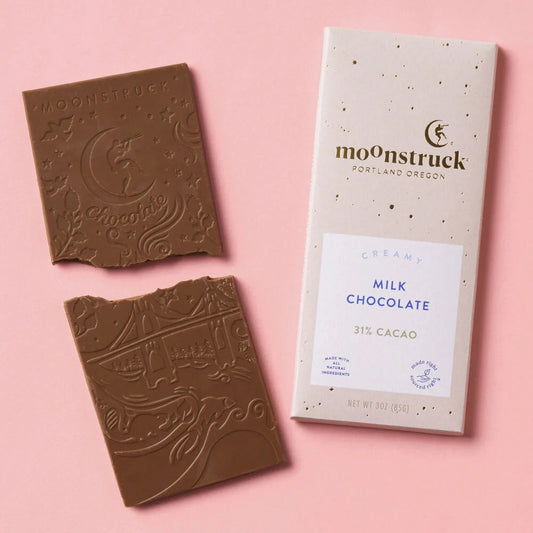 Moonstruck creamy milk chocolate bar with 31 percent cacao beside packaging on pink background hygge pamper gift box