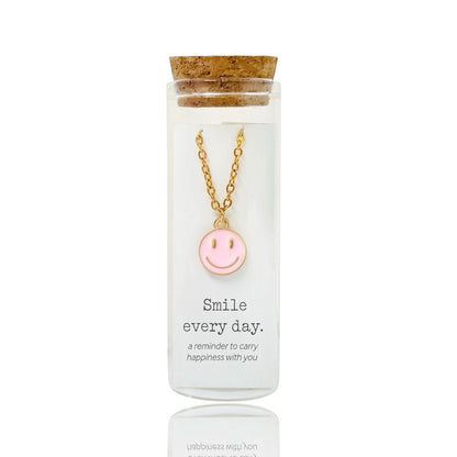 Gold necklace with a pink smiley face pendant in a glass bottle by Dabble Doll