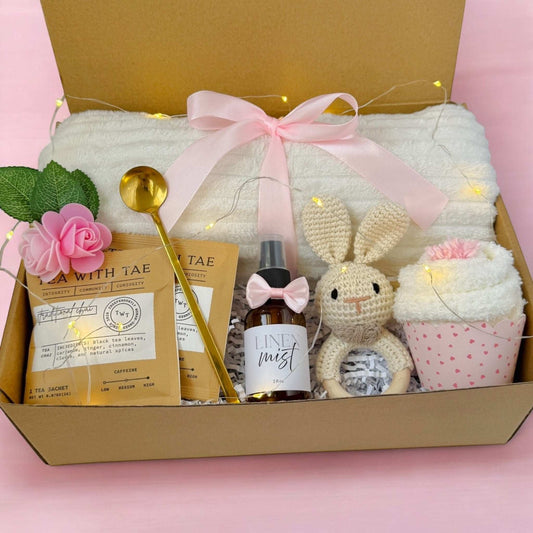 Dabble Doll new mom gift box with tea packets, golden spoon, linen mist, knitted bunny, towel, and cupcake washcloth