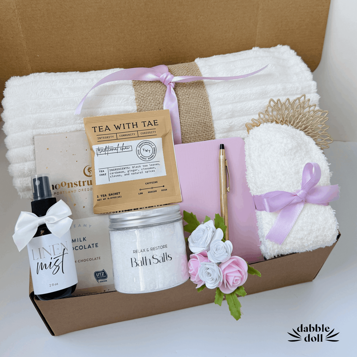 Thoughtful hygge gift basket by Dabble Doll with cozy towel, bath salts, tea sachet, linen mist, chocolate, and sleep mask