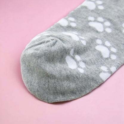 Close up of cute gray cat socks with white paw prints on a pink background